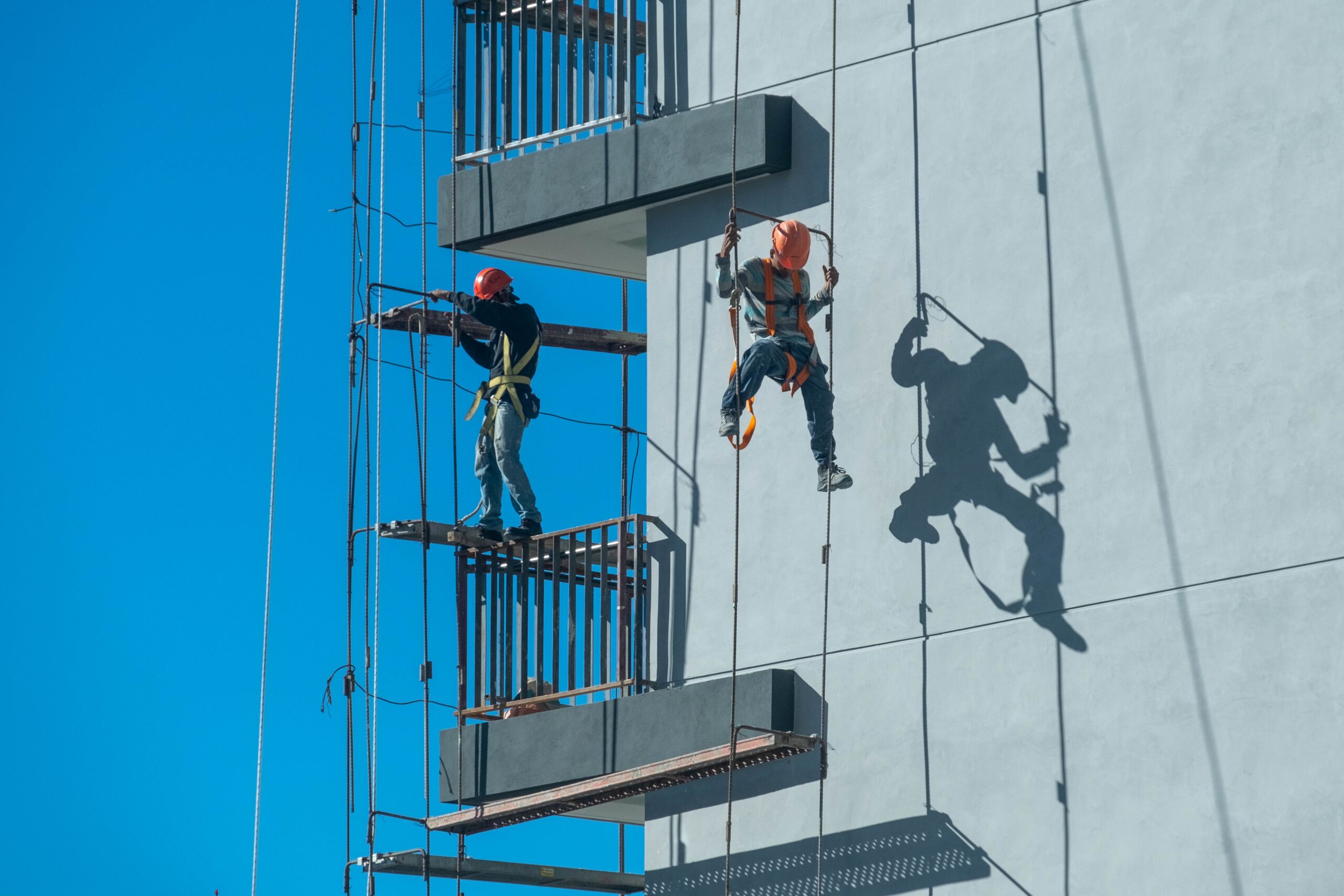 Rope access technicians wearing safety harnesses working on a high-rise building exterior, providing professional facade maintenance and high-rise cleaning services.